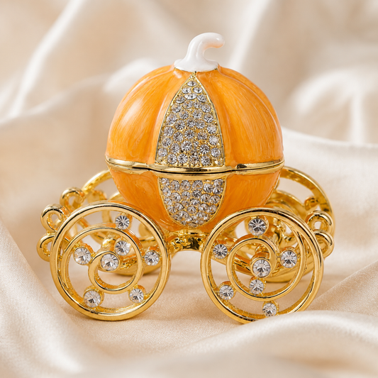Enchanted Pumpkin Carriage Jewellery Box in orange with gold wheels and crystal details resting on soft cream satin fabric.