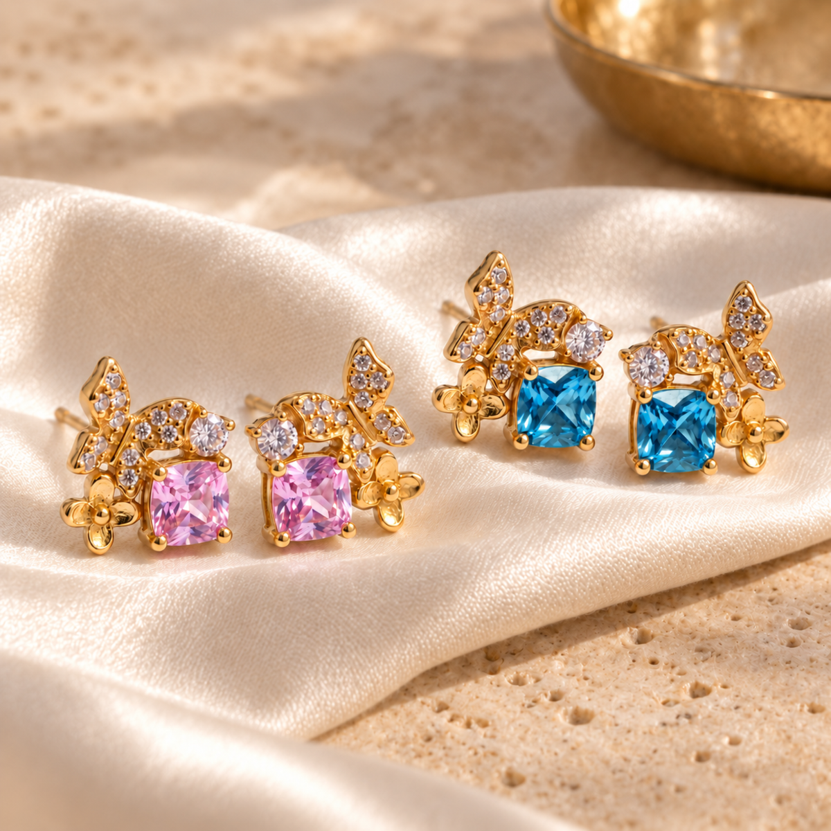 Pink and blue Gold Butterfly Garden stud earrings arranged on champagne satin