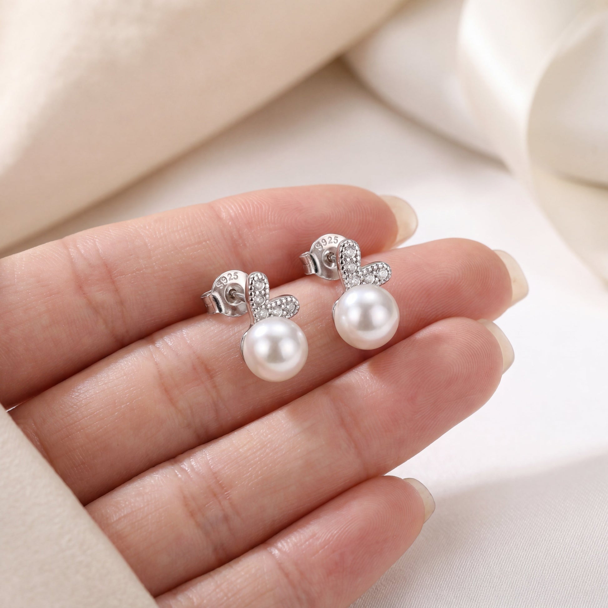 925 sterling silver pearl bunny stud earrings shown in hand to display small size and delicate pearl design