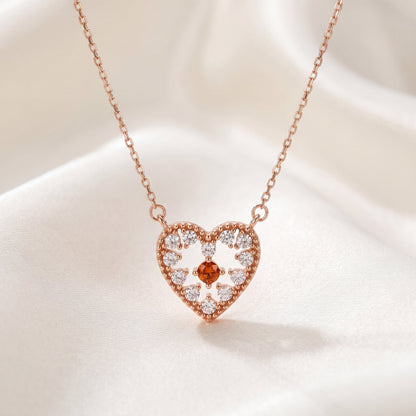 Rose gold 925 sterling silver heart pendant necklace with red centre stone displayed on white silk