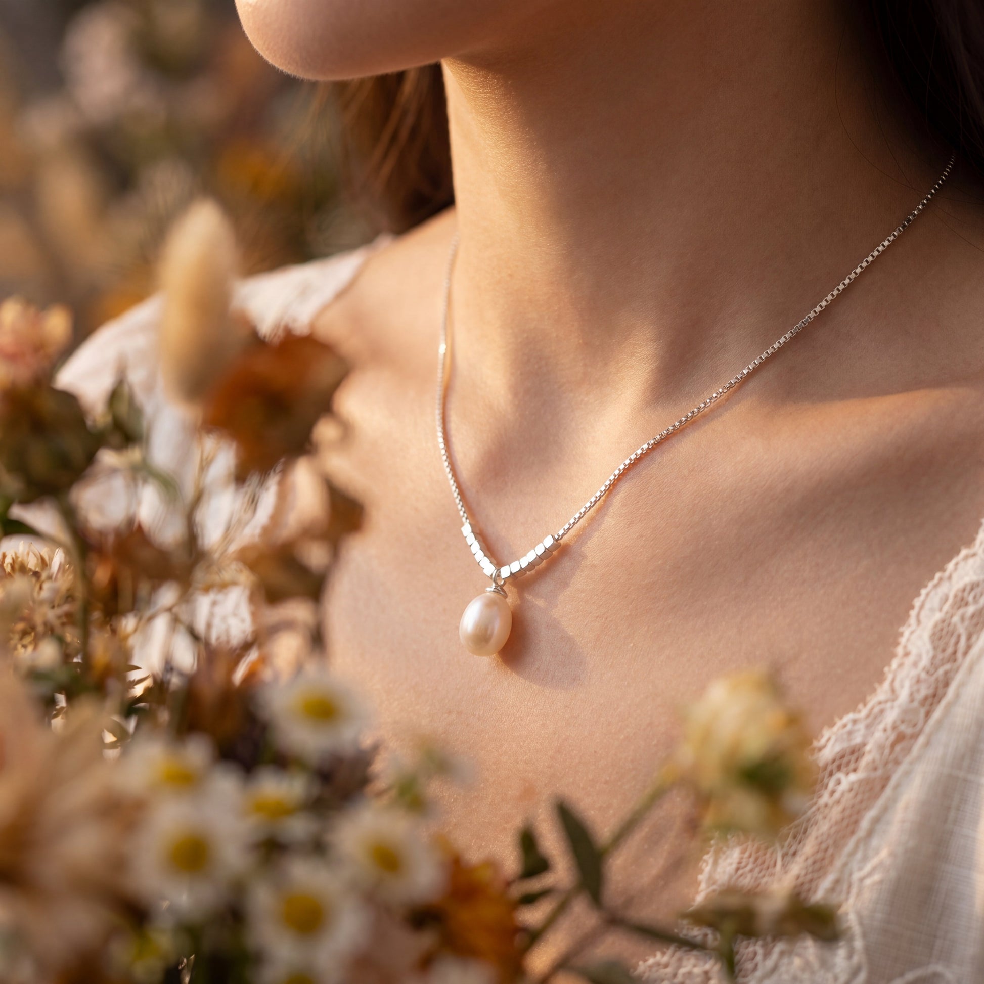 Woman wearing 925 sterling silver teardrop pearl pendant necklace with a soft floral outfit