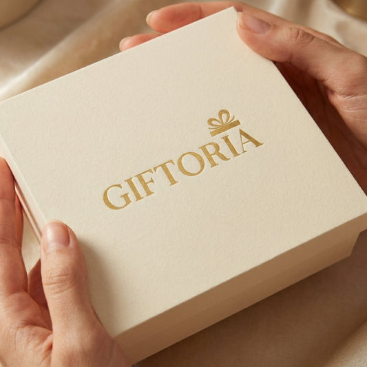 Giftoria luxury cream gift box with gold foil logo held in hands, elegant premium gift packaging