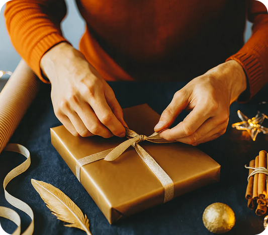 Person wrapping a gift with brown paper and ribbon on a dark surface.