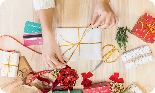 Person wrapping a gift with decorative ribbons and bows on a wooden table.