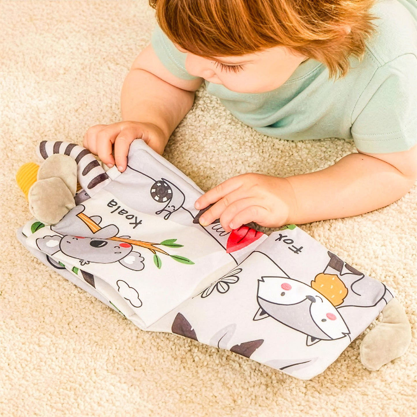 Baby playing with sensory cloth book featuring koala and fox
