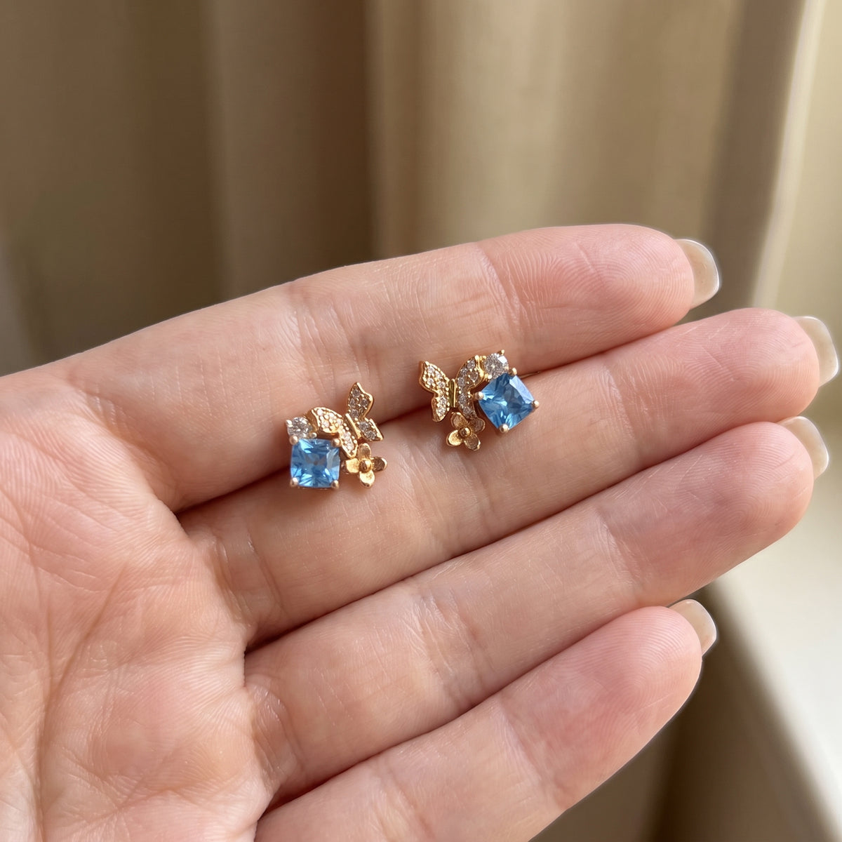Blue Gold Butterfly Garden stud earrings held in hand to show their size