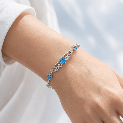 Blue cubic zirconia angel wings heart bracelet worn on a woman’s wrist