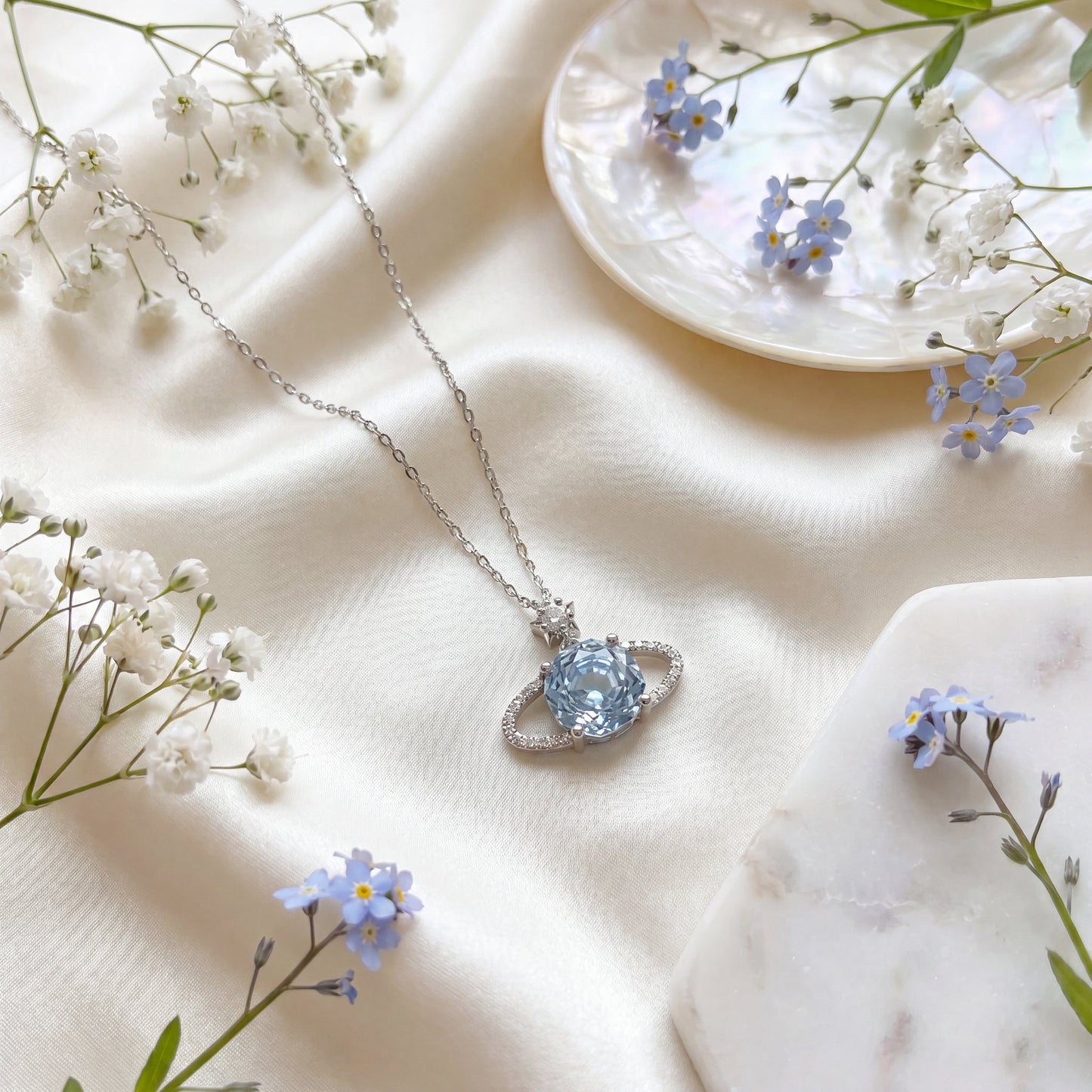 Blue planet star necklace styled on soft fabric with delicate flowers
