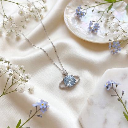 Blue planet star necklace styled on soft fabric with delicate flowers