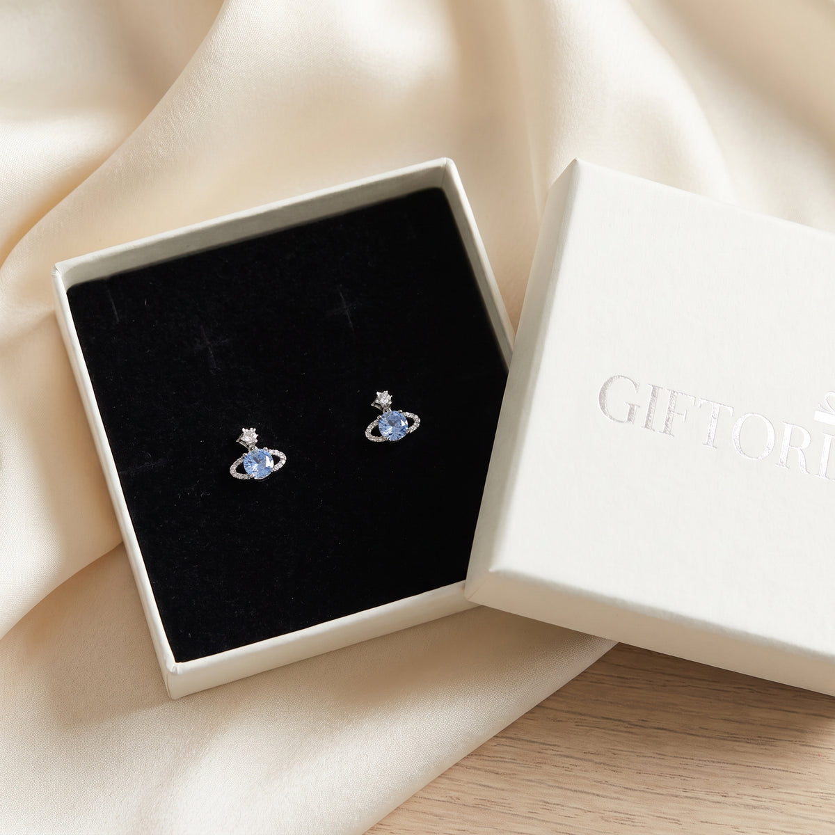 Blue Rose Saturn silver stud earrings in an open cream gift box on cream satin.