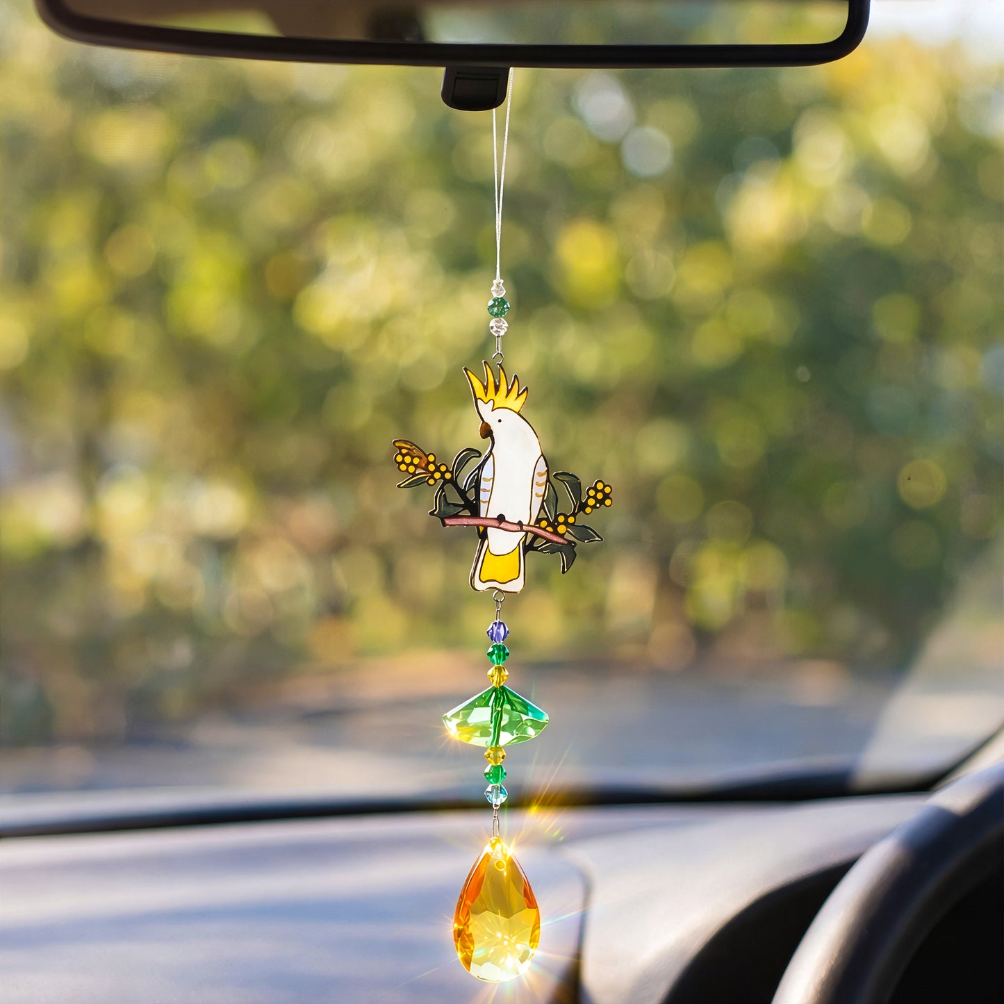Cockatoo crystal sun catcher hanging from car mirror, catching sunlight while driving