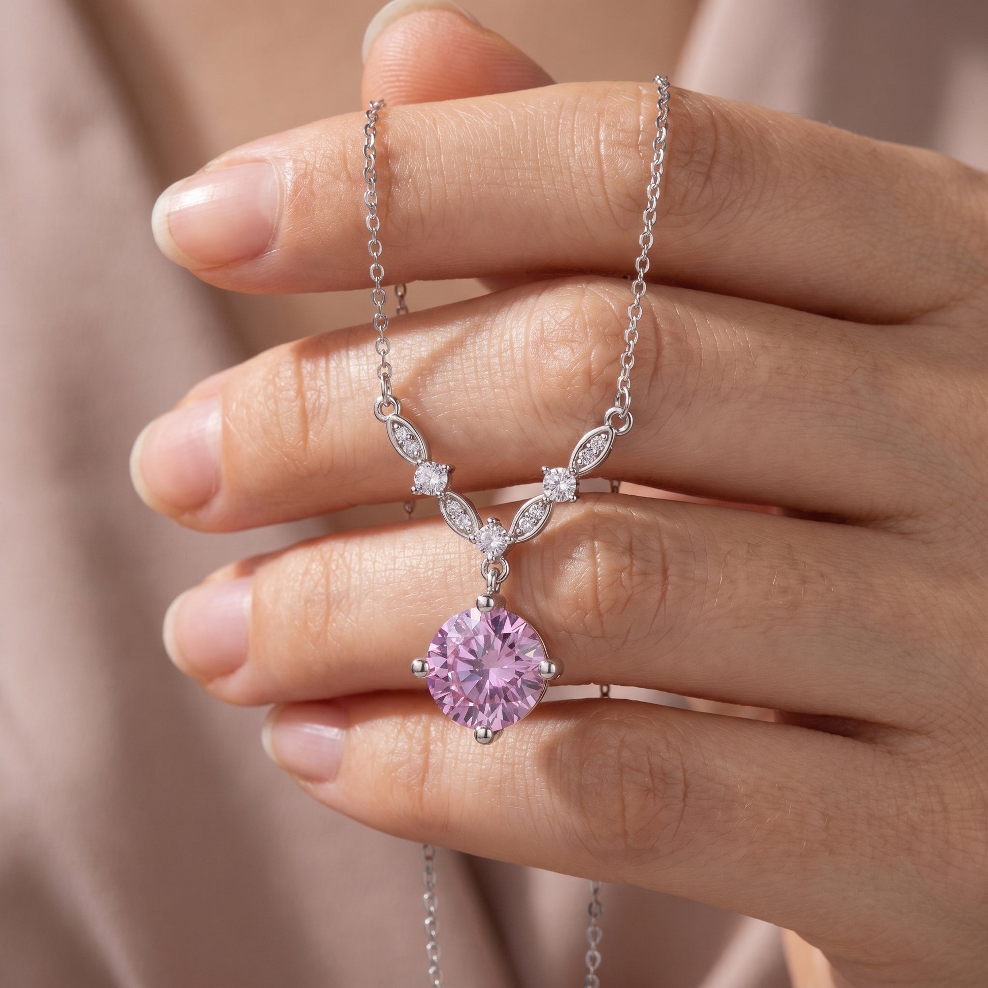 Delicate pink cubic zirconia necklace displayed on hand with floral vine design