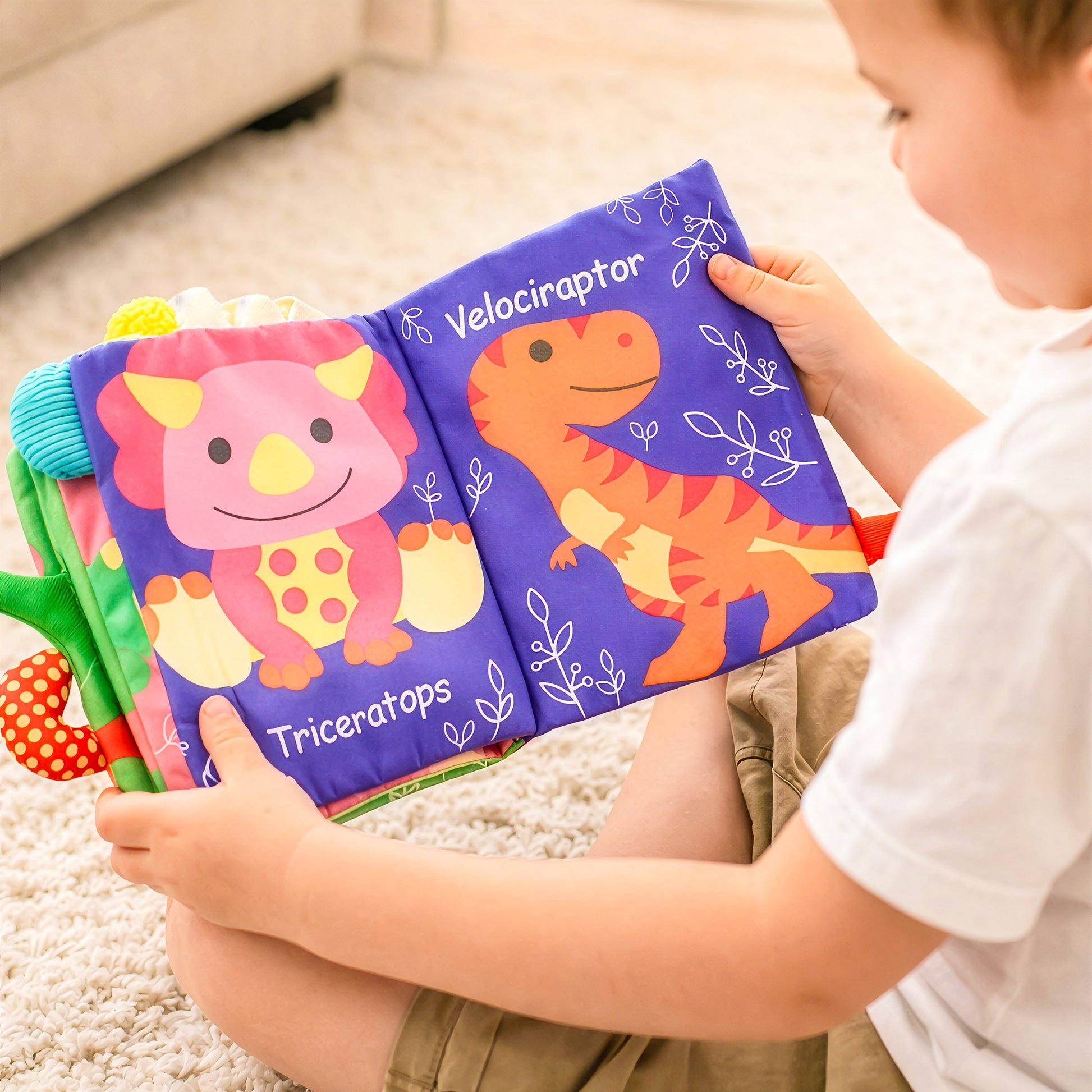 Baby playing with dinosaur cloth book featuring triceratops and velociraptor