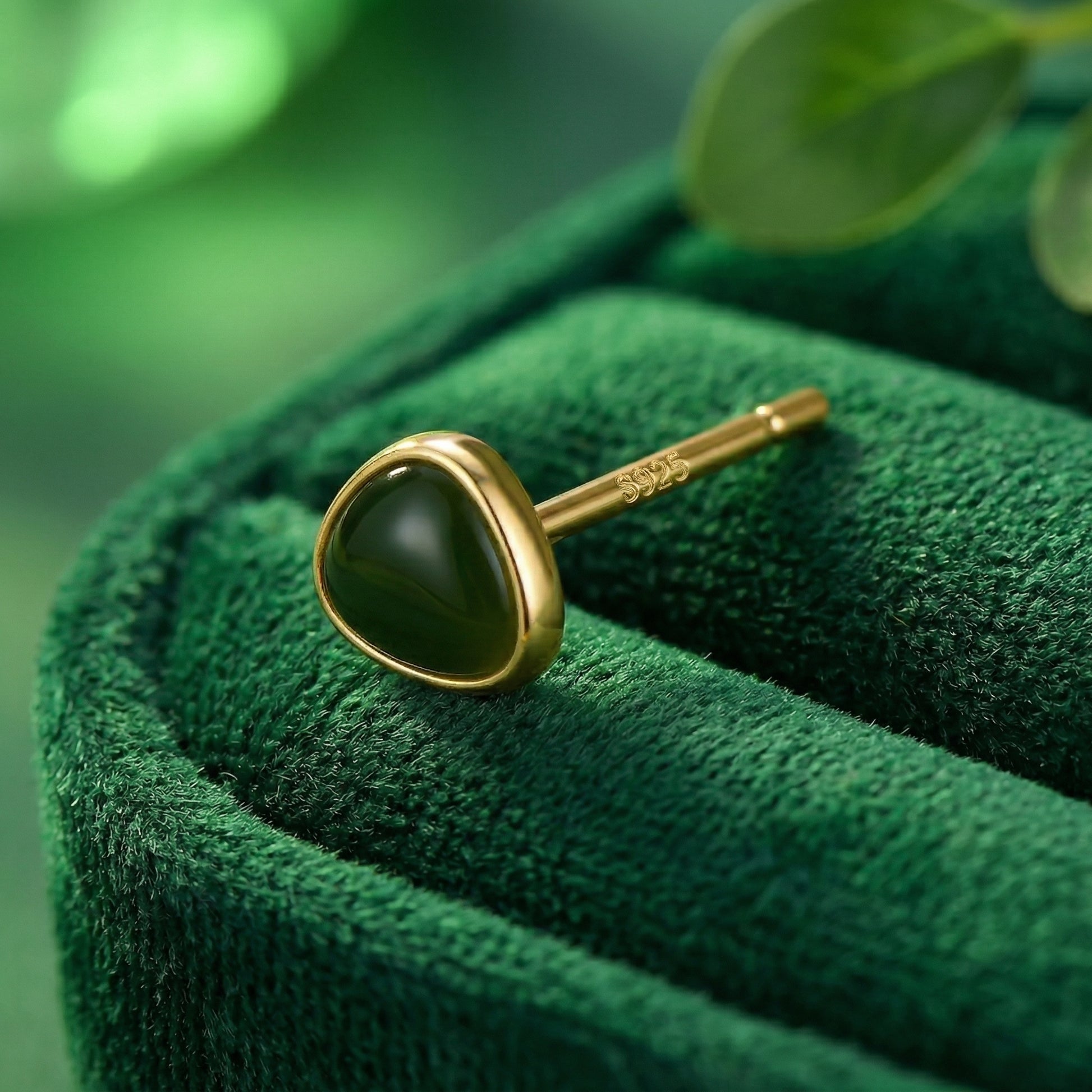 Gold tone 925 sterling silver avocado green stud earrings close up on green velvet fabric