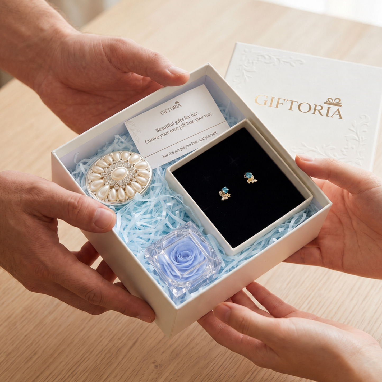 Hands presenting a Giftoria gift box with gold butterfly earrings, blue preserved rose and pearl jewellery box