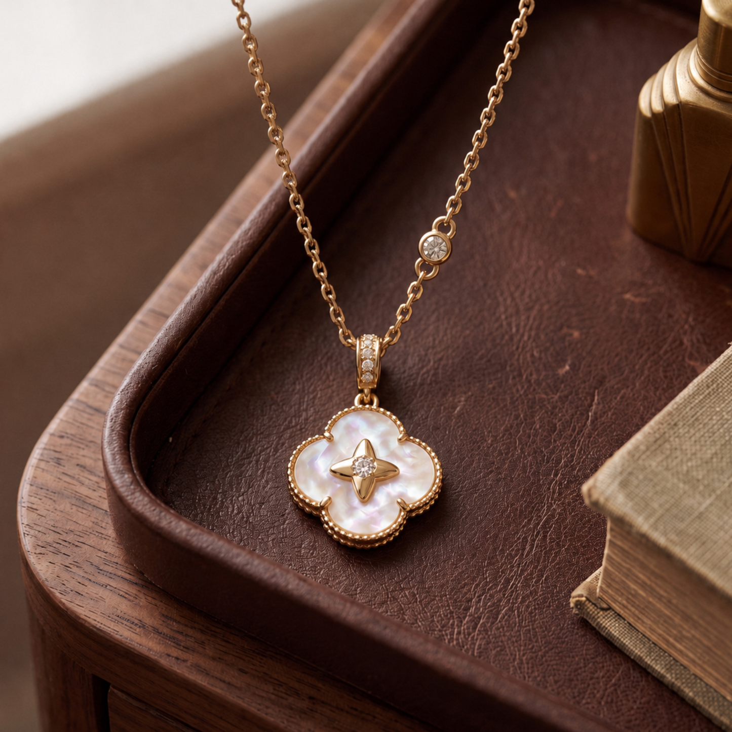 A gold-tone necklace with a four-petal pendant made of iridescent mother-of-pearl and a small gold star in the center, displayed on a dark brown leather tray.