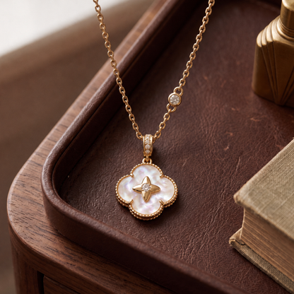 A gold-tone necklace with a four-petal pendant made of iridescent mother-of-pearl and a small gold star in the center, displayed on a dark brown leather tray.