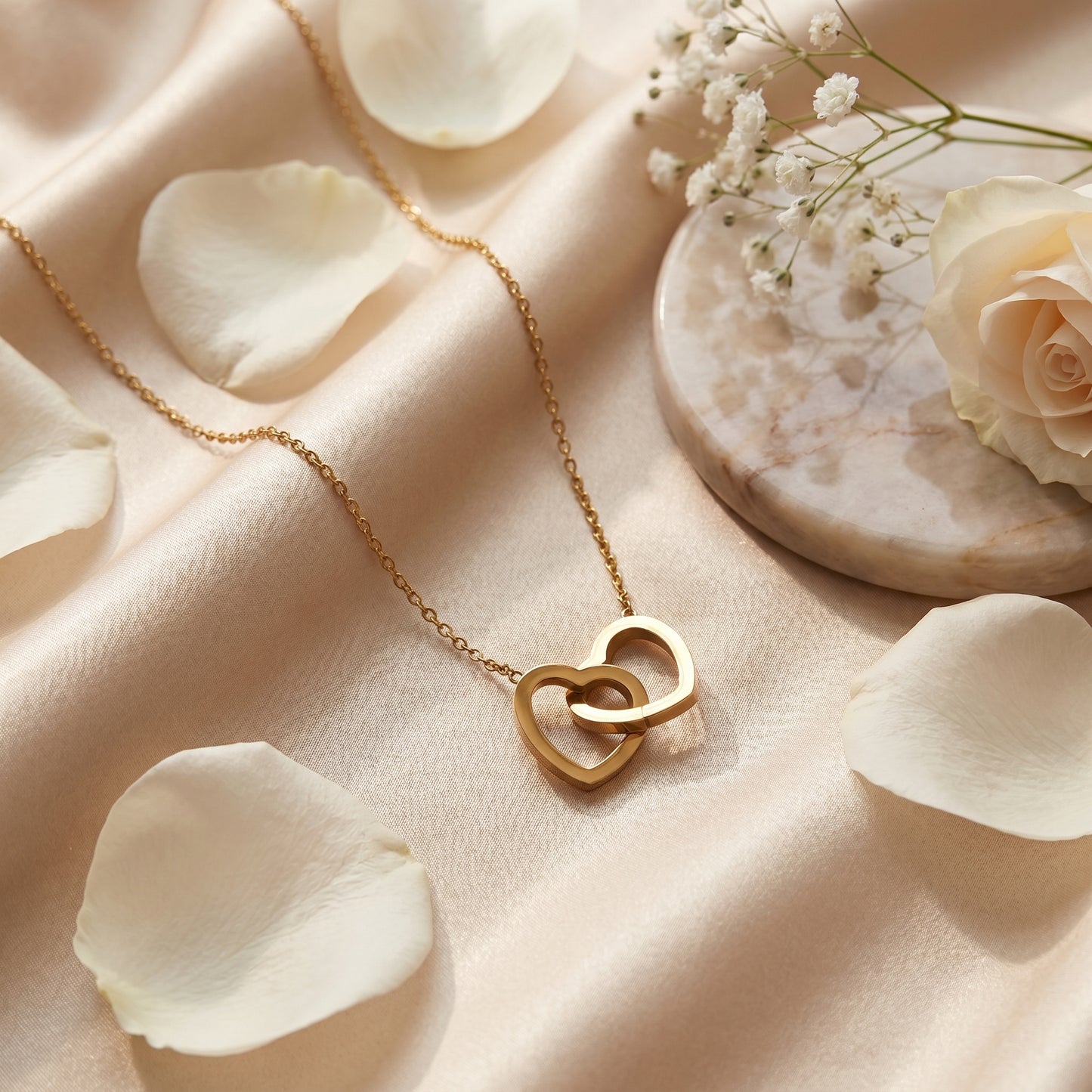 Gold double linked heart necklace arranged with white flower petals for a romantic anniversary gift