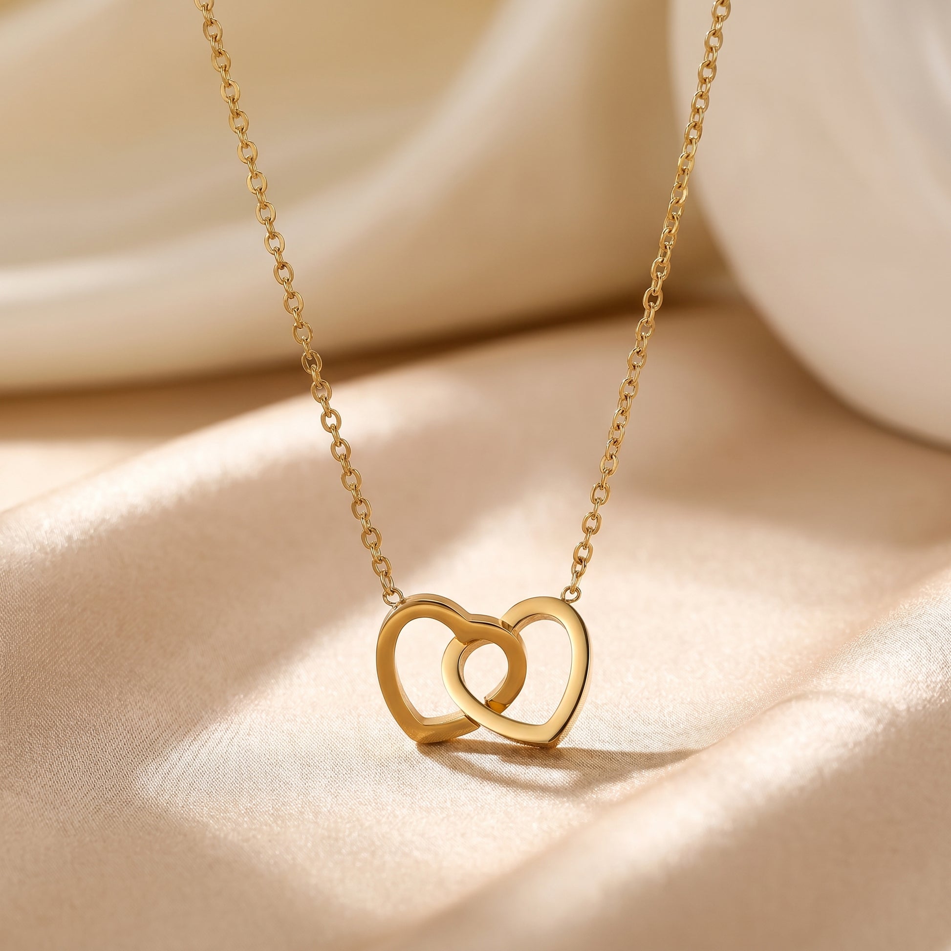 Gold interlocking double heart necklace styled on champagne satin as a romantic jewellery gift for her