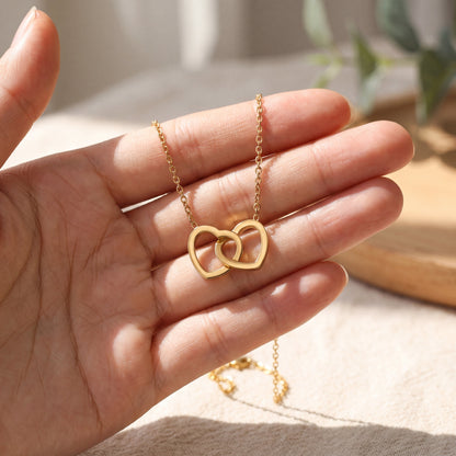Gold double linked heart necklace held in hand to show the pendant size, chain detail and polished finish
