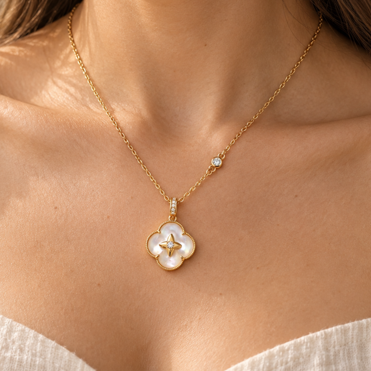 A close-up of a model wearing a delicate gold chain necklace with a four-petal clover pendant made of white mother-of-pearl and a small gold star in the center, accented by a small clear stone on the chain.