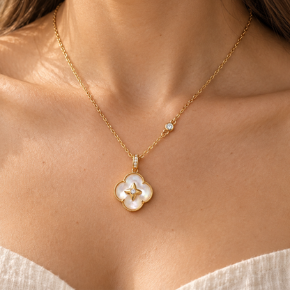 A close-up of a model wearing a delicate gold chain necklace with a four-petal clover pendant made of white mother-of-pearl and a small gold star in the center, accented by a small clear stone on the chain.