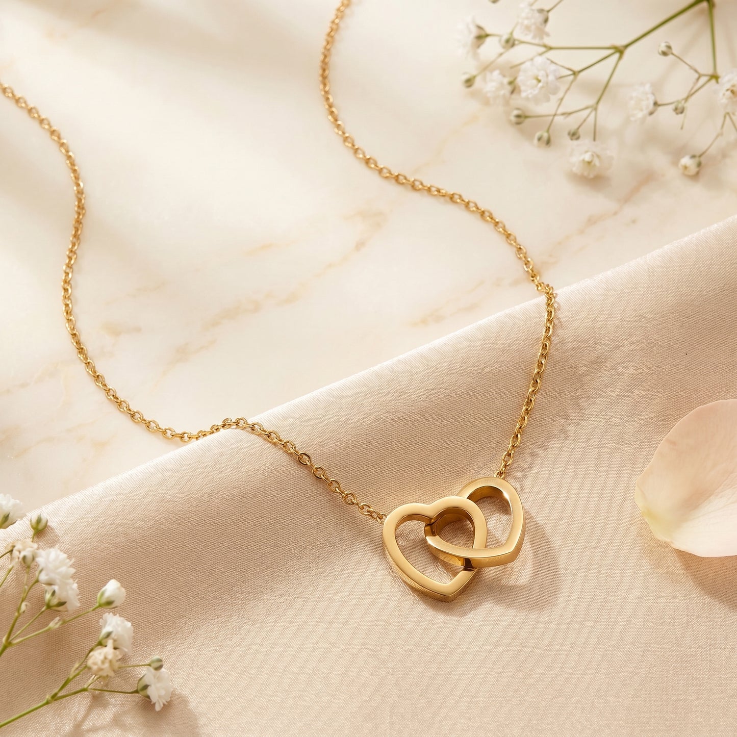 Full view of a gold stainless steel double heart pendant necklace with its delicate chain on cream satin