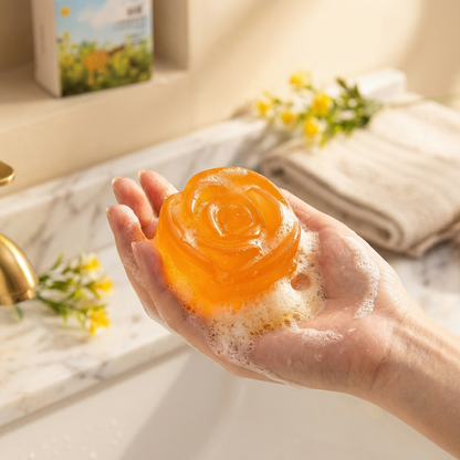 Handmade floral essential oil soap in orange honey shape with creamy foam in hand during use.