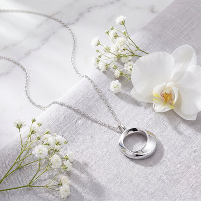 Modern sterling silver circle pendant necklace arranged on soft silver satin fabric
