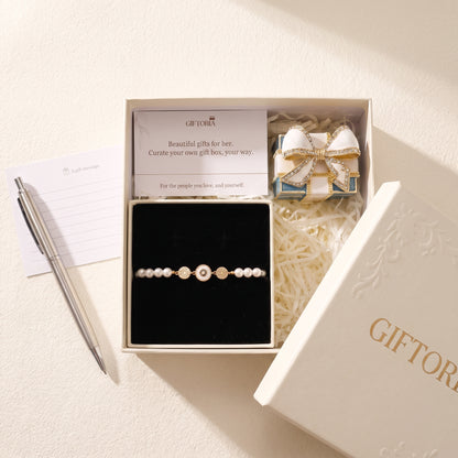 Gold evil eye pearl bracelet gift set beside a personal message card and Giftoria gift box
