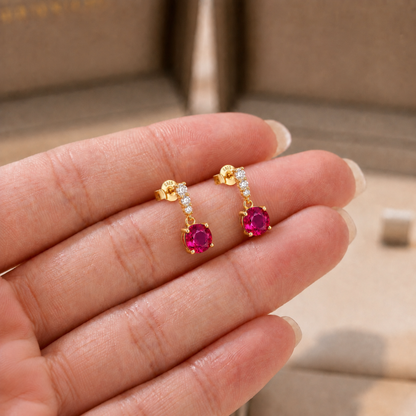 Petite ruby red drop earrings shown in hand for size reference