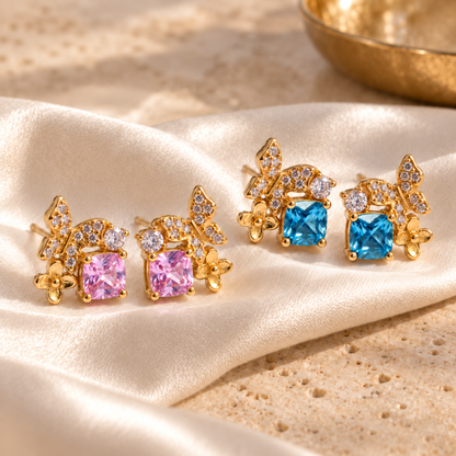 Pink and blue Gold Butterfly Garden stud earrings arranged on champagne satin