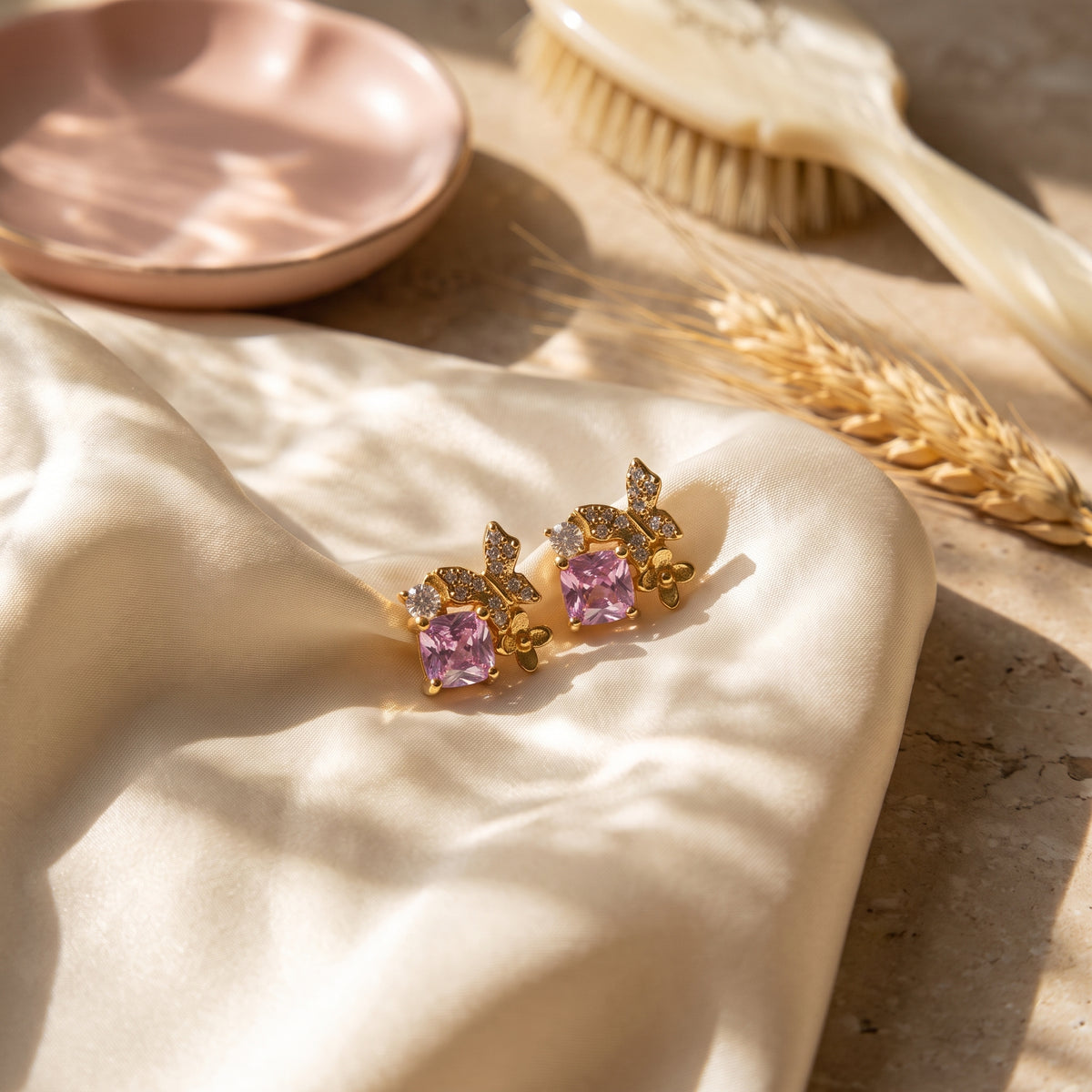 Pink Gold Butterfly Garden stud earrings displayed on soft champagne satin