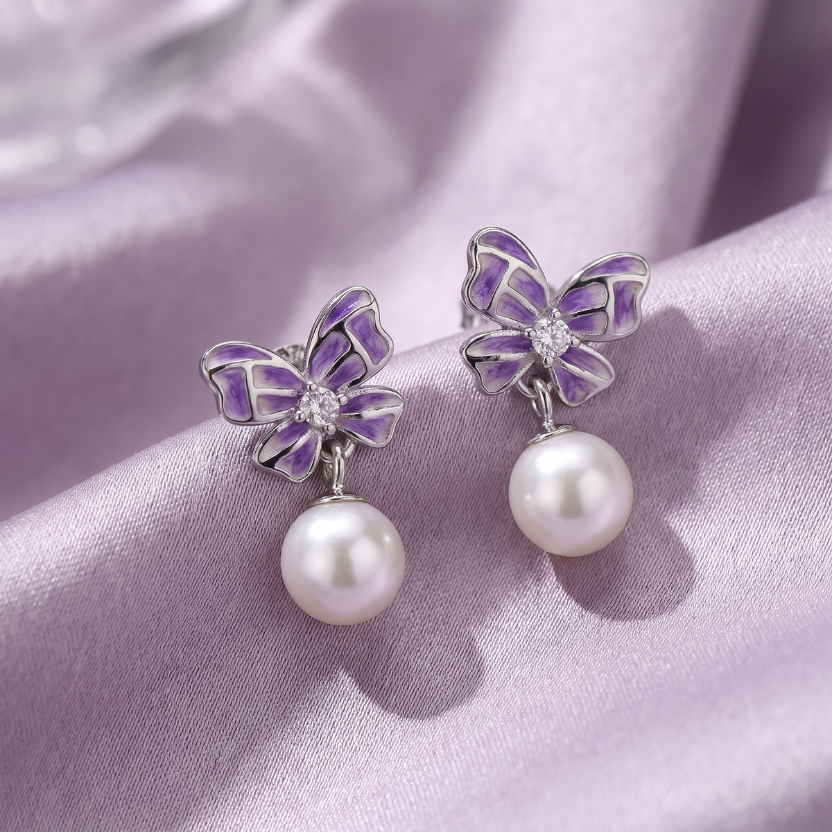 Close-up of purple butterfly pearl drop earrings on soft lilac satin