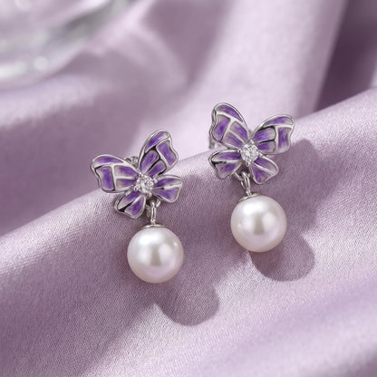 Close-up of purple butterfly pearl drop earrings on soft lilac satin
