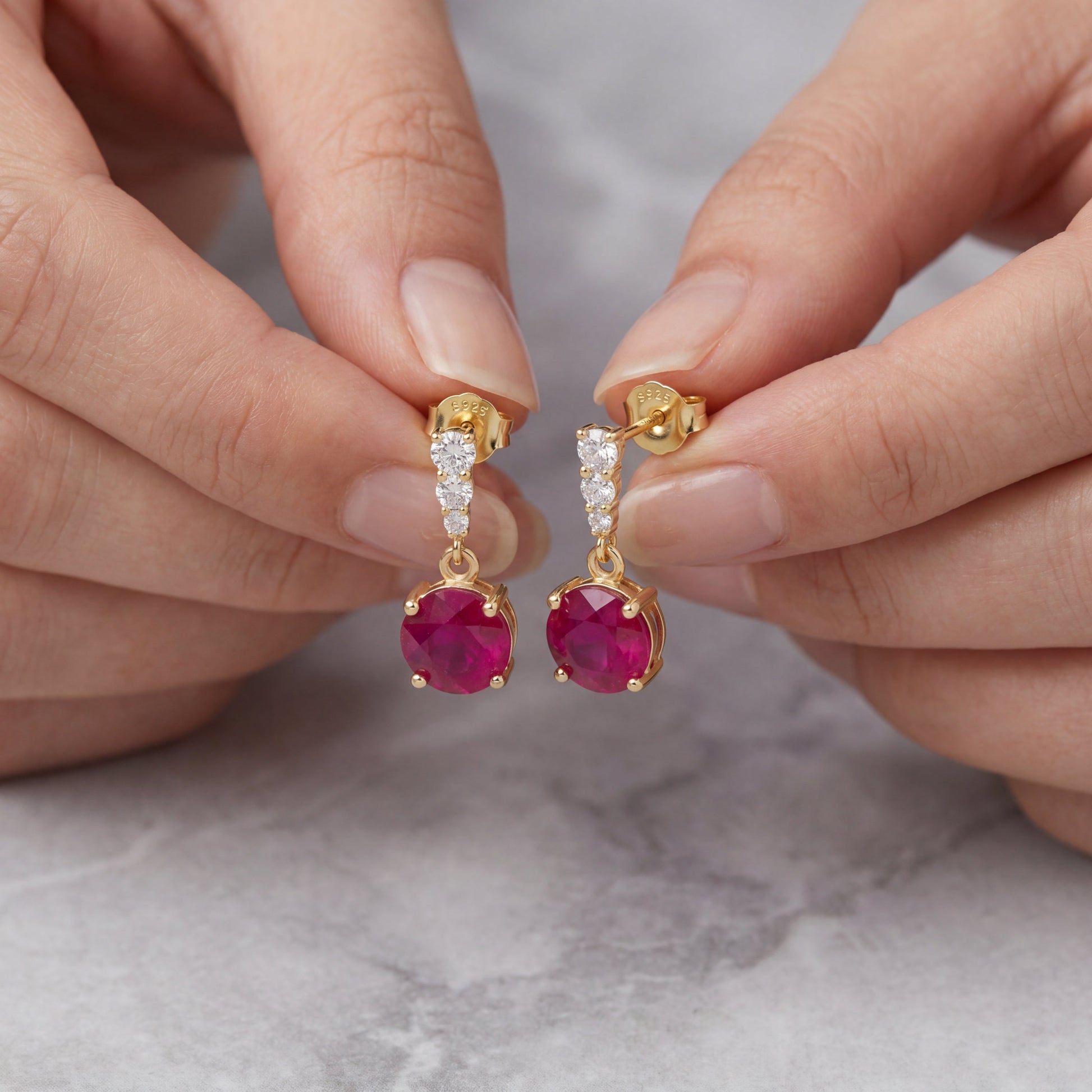 Hand holding 18K gold plated 925 sterling silver red cubic zirconia drop stud earrings detail