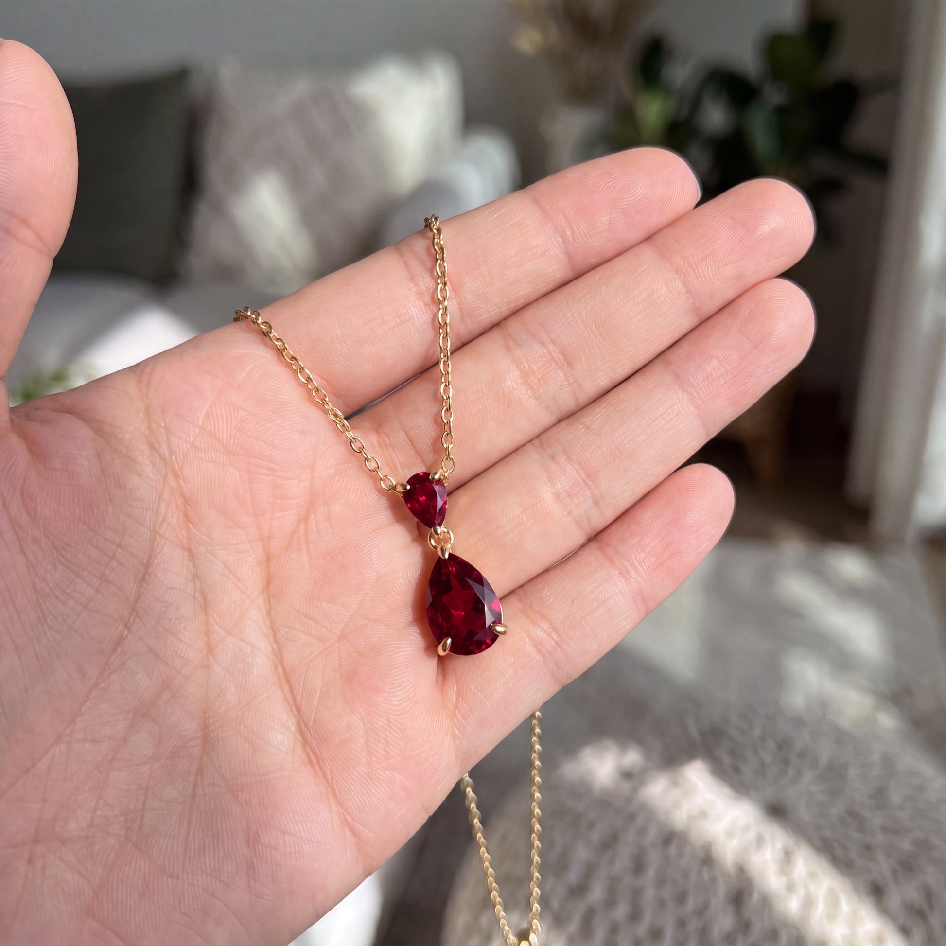 Red teardrop pendant necklace shown in hand for size reference