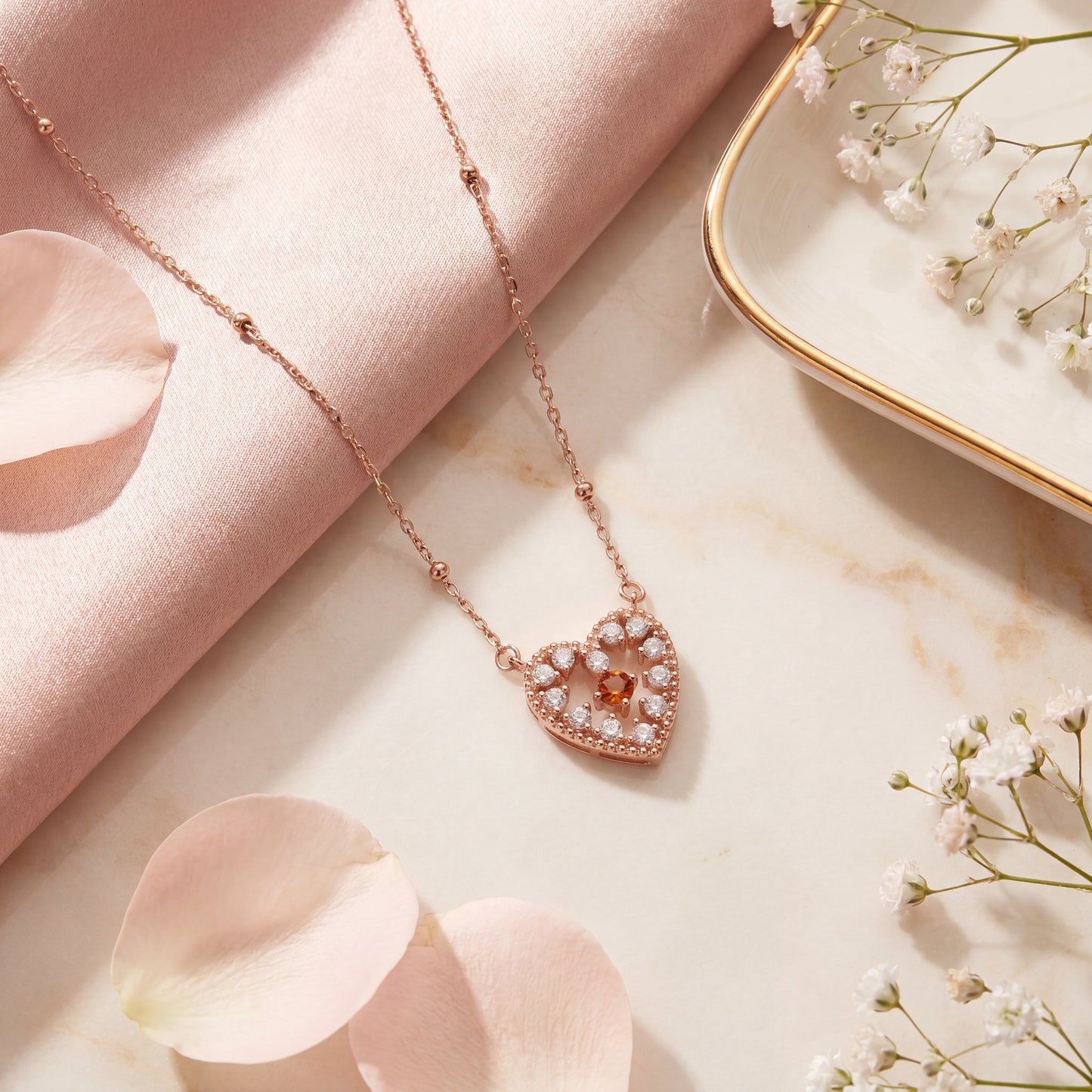 Rose gold red sparkle heart necklace styled on pink satin with flower petals as a romantic gift for her