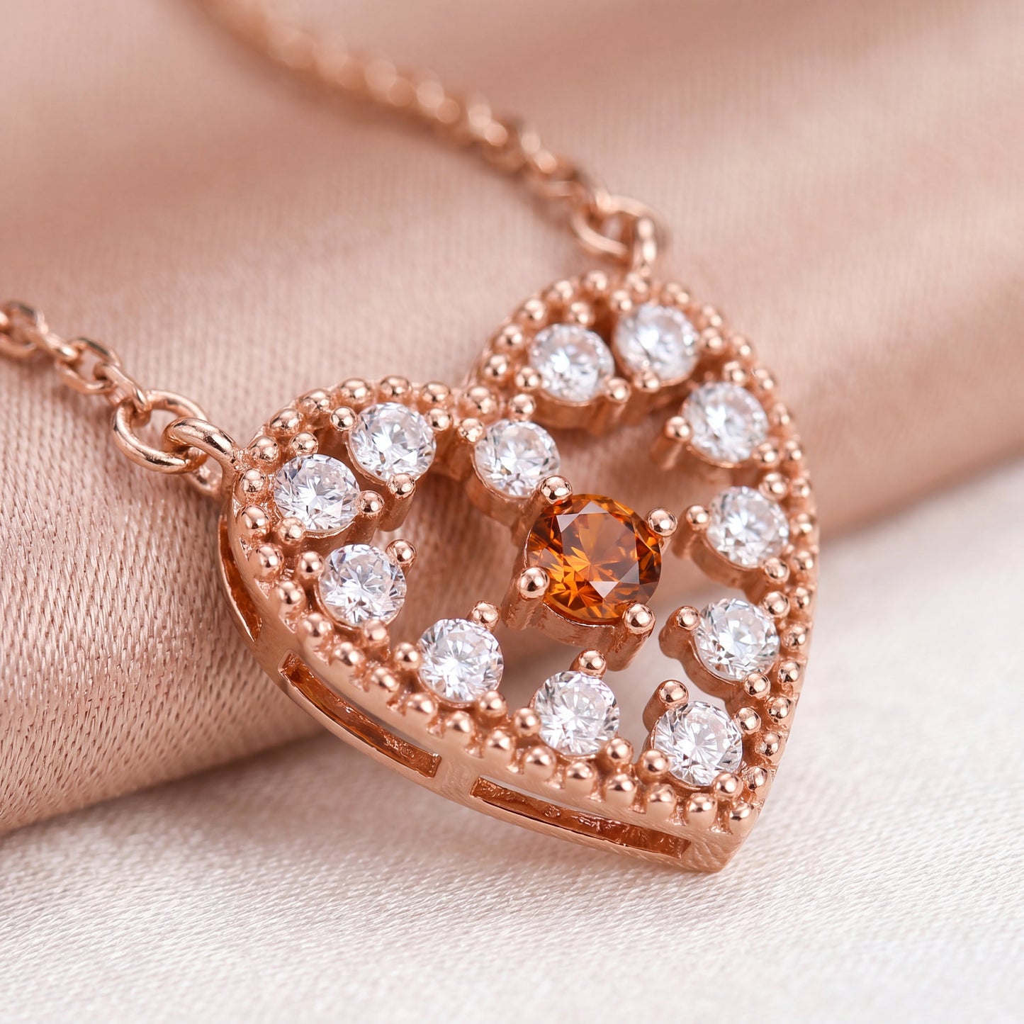 Close-up of a rose gold heart pendant with clear sparkle stones and a red centre stone