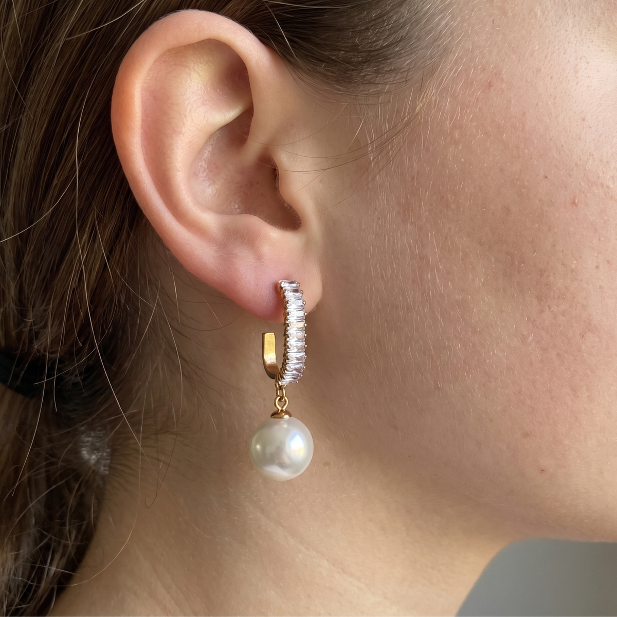 Side view of a woman wearing sparkling gold-tone baguette pearl drop earrings