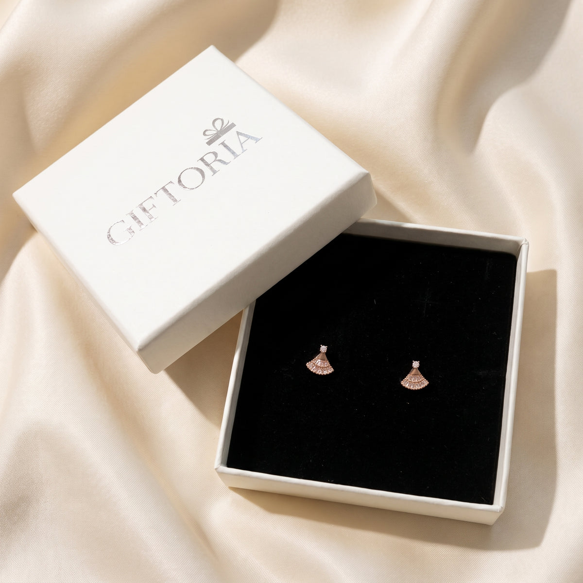 Rose gold fan-shaped earrings displayed in a black jewellery box beside Giftoria packaging.