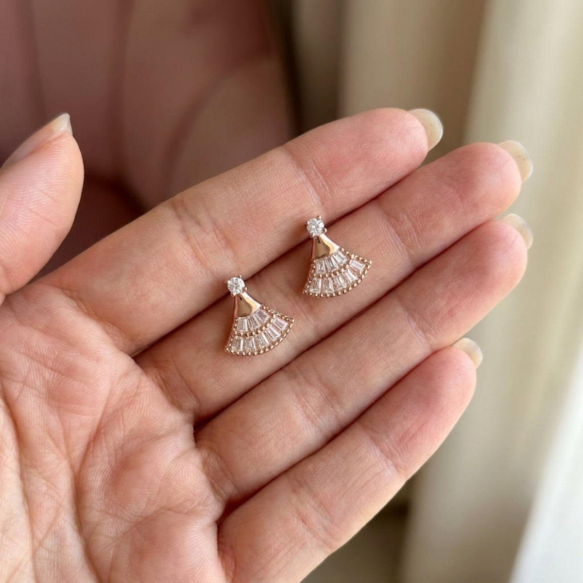 Pair of rose gold fan-shaped moissanite earrings resting on a hand.