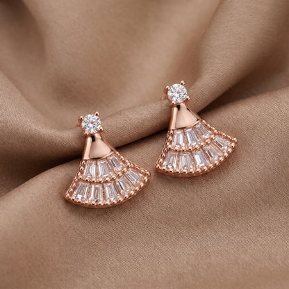 Rose gold fan-shaped drop earrings with clear baguette and round stones, displayed on draped brown fabric.