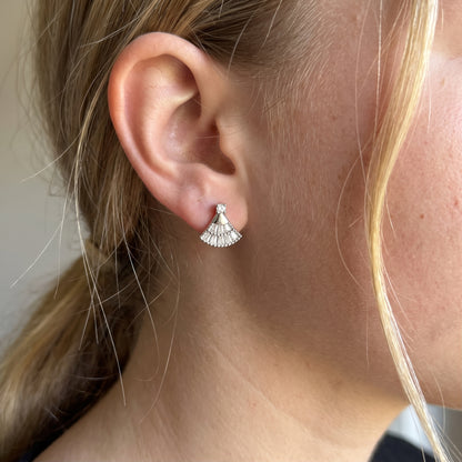 Silver fan-shaped moissanite stud earring worn on an ear, showing its size and shape.