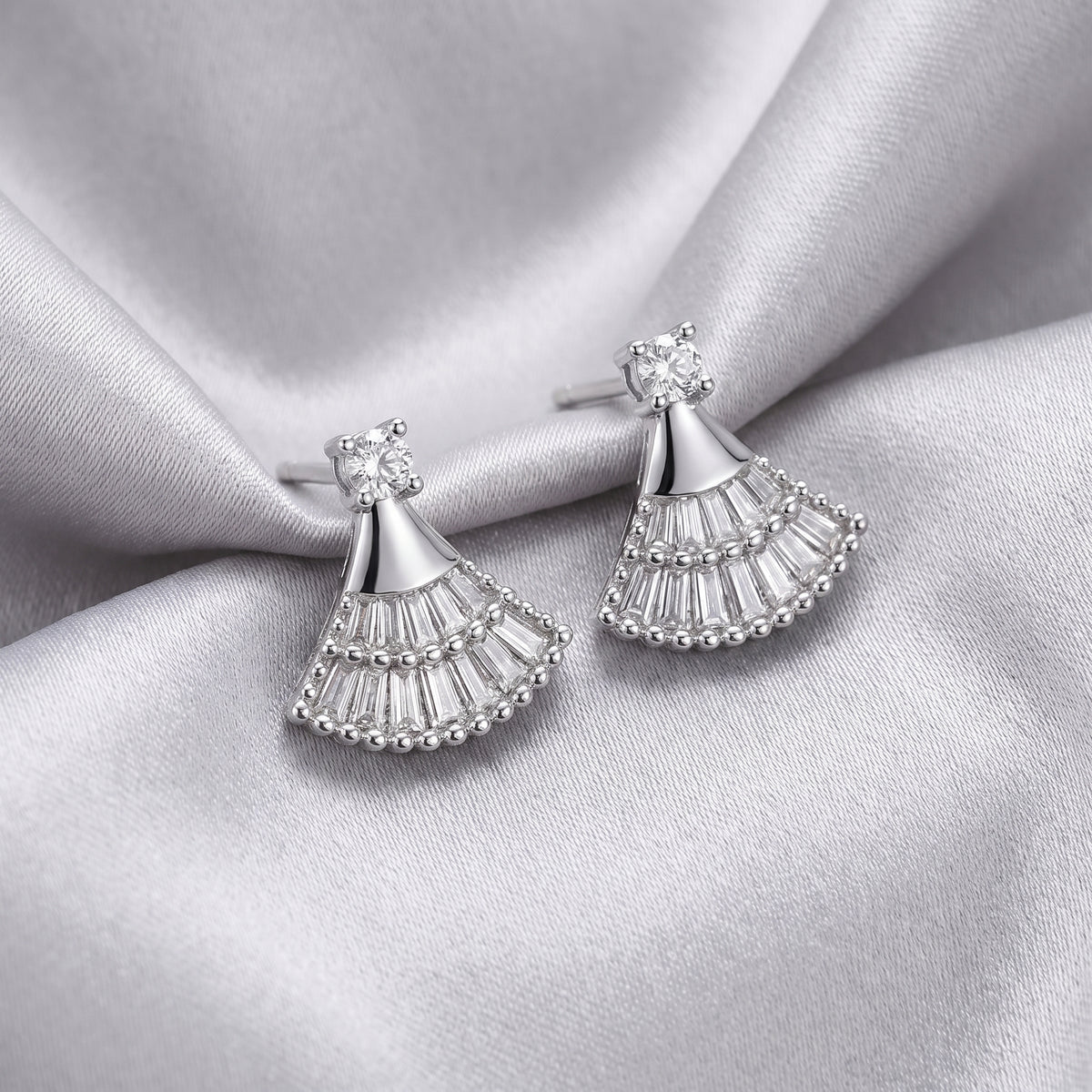 Silver fan-shaped earrings on silver satin