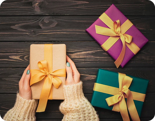 Three gift boxes with gold ribbons on a wooden surface, one held by a person.